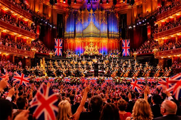 View from the stalls across a flag-waving arena audience to an orchestra in a grand concert hall